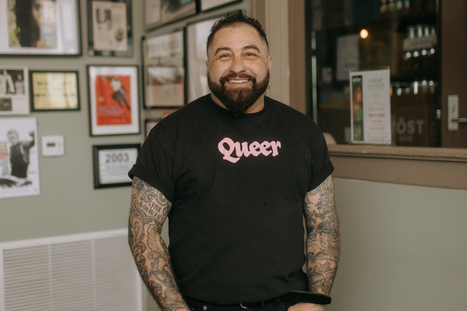 Wearing a prominent "Queer" shirt, Mason Gallo is all smiles inside Queens' Provisions in downtown Flint on May 4, 2024.